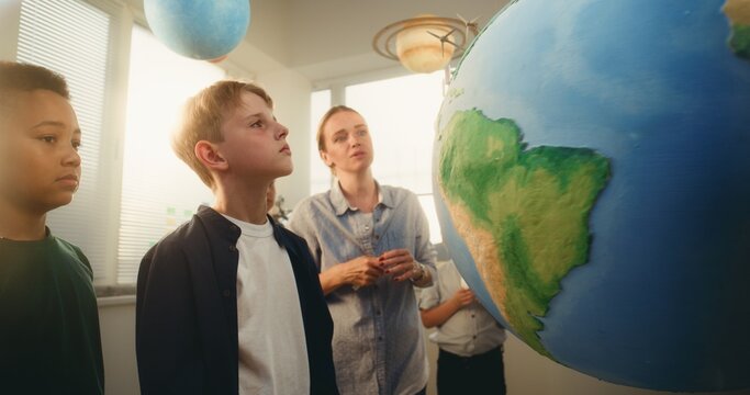 STEM Science Lesson: Female Teacher Educating Smart Diverse Kids Using Globe with Miniature 3D Models of Wind Turbines and Solar Panels. Primary School Children Studying Renewable Energy and Ecology.