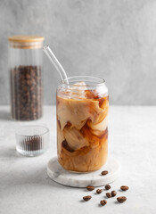 Ice latte coffee in a glass with milk on a marble board on a  light background with coffee beans.