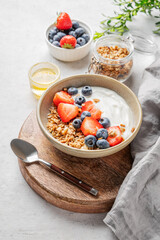 Natural yogurt with granola, blueberry and strawberry in a bowl on a wooden board on a light background