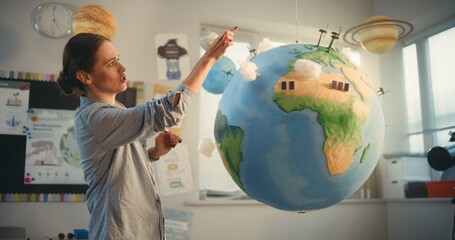 STEM Class: Female School Teacher Educating Science and Renewable Energy Sources Using Model of Planet Earth in Classroom. Miniature 3D Models of Wind Turbines and Solar Panels on Globe. Medium Shot.