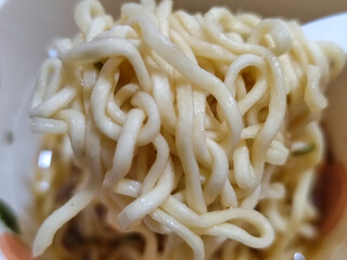 Rolls of springy white instant noodles are lifted with a fork from the bowl, highlighting their...