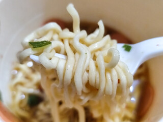 Rolls of springy white instant noodles are lifted with a fork from the bowl, highlighting their...