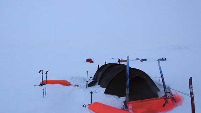 Pan across snowy white winter camp scene with tents, skis, copy space