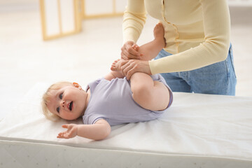 Mother playing with her cute baby on changing table at home, closeup