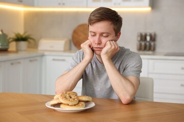 Gluten free diet. Sad woman with pretzels at wooden table in kitchen