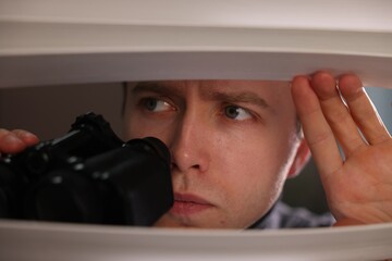 Paranoia. Worried man with binoculars looking through window blinds indoors
