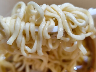 Rolls of springy white instant noodles are lifted with a fork from the bowl, highlighting their...