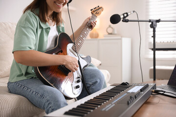 Smiling woman working with MIDI keyboard and guitar at table in home studio, closeup