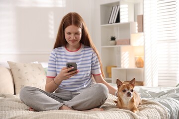 Teenage girl using smartphone and dog on bed at home