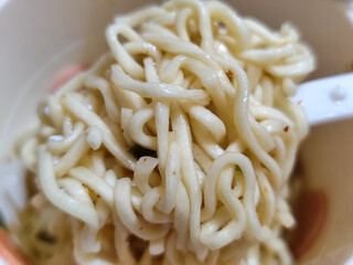 Rolls of springy white instant noodles are lifted with a fork from the bowl, highlighting their...