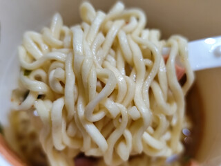 Rolls of springy white instant noodles are lifted with a fork from the bowl, highlighting their...