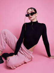 A woman in a pink hoodie and sweatpants poses for a photo. The pink color of her outfit gives off a...