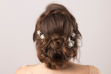 Naklejka premium Elegant bridal tiara adorning the meticulously styled hair of a young bride, seen from behind, against a soft grey studio backdrop