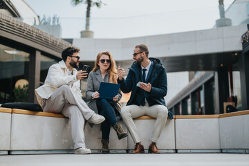Fototapeta premium Business people are collaborate on a project while sitting in an outdoor. The group appears engaged, using devices and documents, reflecting teamwork, creativity, and a productive collaboration.