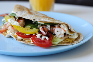Detailed view of folded egg tortilla wrap featuring juicy shrimp, melted cheese, ripe avocado and fresh greens. Tasty and nutritious breakfast in close-up