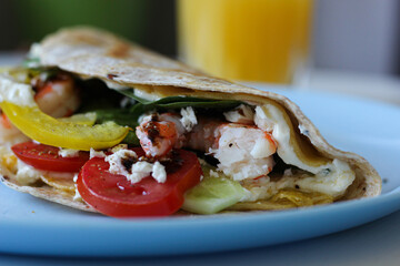 Macro shot of egg-layered tortilla wrap filled with shrimp, feta, cherry tomatoes and avocado. Creamy and colorful ingredients captured in delicious detail