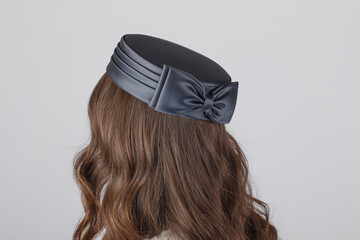 Elegant wedding hat worn by a young girl, seen from behind, set against a smooth grey studio...