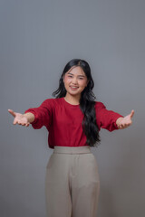 Young Indonesian woman with long black hair, smiling and gesturing with outstretched arms. Wearing...