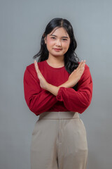 Obraz premium Young Indonesian woman wearing a red top and beige pants, crossing her arms in a 