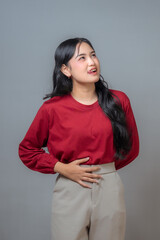 An Indonesian woman in a red shirt and beige pants, holding her stomach while sticking her tongue out in a playful expression. Captures a moment of lightheartedness or discomfort.