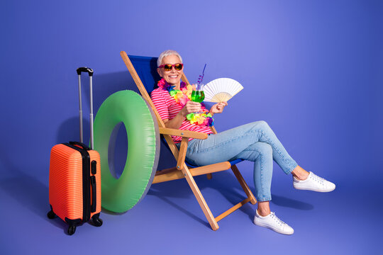 Elderly Woman Enjoying a Relaxing Vacation Vibe with Summer Props on a Violet Background