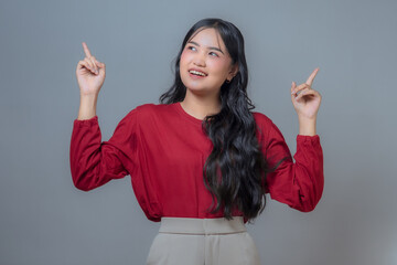 An Indonesian Asian woman in a red long-sleeve shirt and beige pants smiling and pointing upwards...