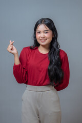 Young Indonesian woman in a red long-sleeve top and beige pants smiling confidently while showing a...