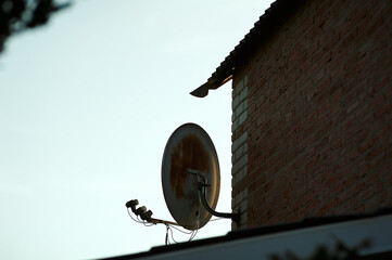 old satellite dish on house against sunset