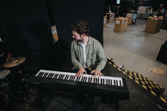A man performs on an electronic keyboard during a band rehearsal in a modern setting. The environment suggests preparation for a concert with musical passion and creative energy.