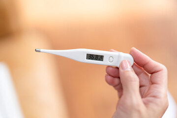 Person checks body temperature using a digital thermometer in a cozy indoor setting during a quiet...