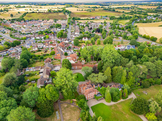 Aerial view of a pretty rural English village seen from a nearby large manor house in the lower part of the image. The distance shows a new housing development and rural Essex, UK countryside.