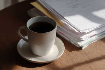 Cup of coffee sits beside stack of papers on wooden table