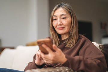 Woman relaxing at home while using smartphone in cozy living room setting during late afternoon