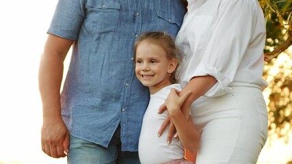 Happy family spending time outdoors standing at sunset in park. Mom, dad and daughter relaxing together in park, mother touching and hugging beloved daughter, close-up. Happy family relationship 