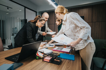 Four coworkers engaged in a team discussion at a conference table in an office setting, working on...