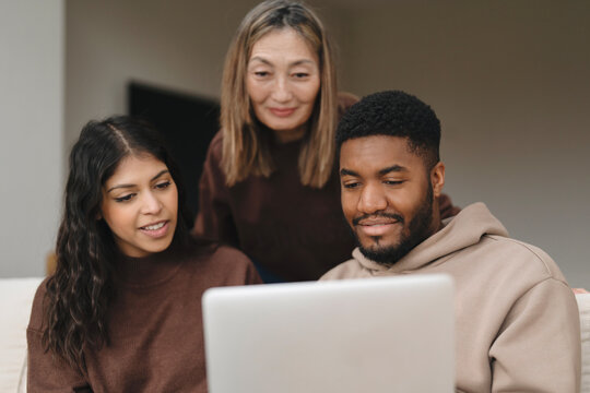 Group of friends enjoying a cozy indoor gathering while using a laptop in a well-lit living room