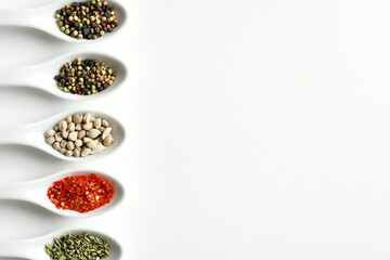 White ceramic spoons in a row, each holding a vibrant, unique spice, creating a colorful and aromatic display on a white background.