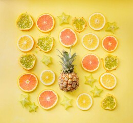 A summer flat lay of sliced citrus fruits and a pineapple on a yellow background.