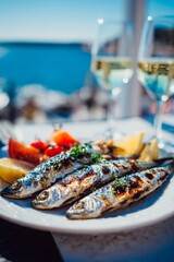 A plate of grilled fish sits on a table, accompanied by fresh tomatoes, lemon, and two glasses of white wine. The beautiful seaside view complements a perfect day