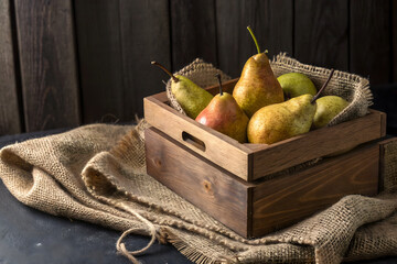 A wooden box is filled with fresh, ripe pears, resting on a burlap cloth