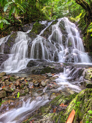 waterfall in the forest, Scenic view of a small waterfall cascading over mossy rocks in a lush tropical forest. Tranquil nature scene with clear flowing water and vibrant greenery.
