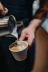 Barista demonstrates their skills by pouring steamed milk into an espresso cup to create intricate latte art design. The focus is on the technique and creativity behind professional coffee preparation