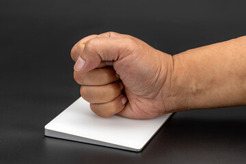 Clenched fist rests on white trackpad against dark background, conveying sense of determination or...