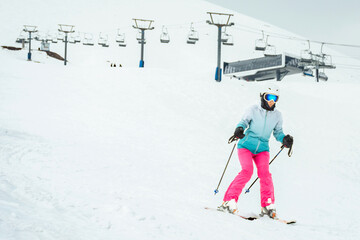 Woman skier in bright clothes skiing slowly on beginner slope with ski lift and station in Gudauri...