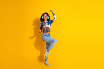 Joyful young woman dancing with headphones on a vibrant yellow background expressing fun and...