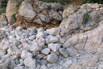 Pile of white and gray coastal rocks and boulders at the base of a rugged cliff, captured in...