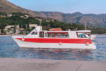 Tourist boat docked near coastal town with passengers on board. Mountains and buildings visible in...