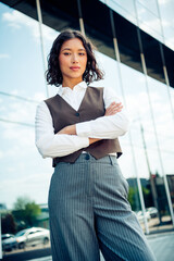 Confident businesswoman in modern office attire posing against urban glass building on a sunny day