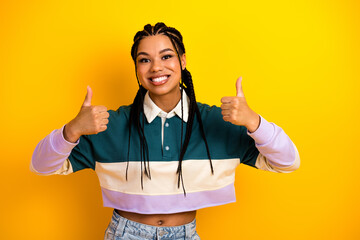 Happy young woman with braided hair showing thumbs up on bright yellow background promoting...