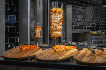 Shawarma Grill and Pizza Display. Vertical meat rotisseries with sliced shawarma beside fresh cut...